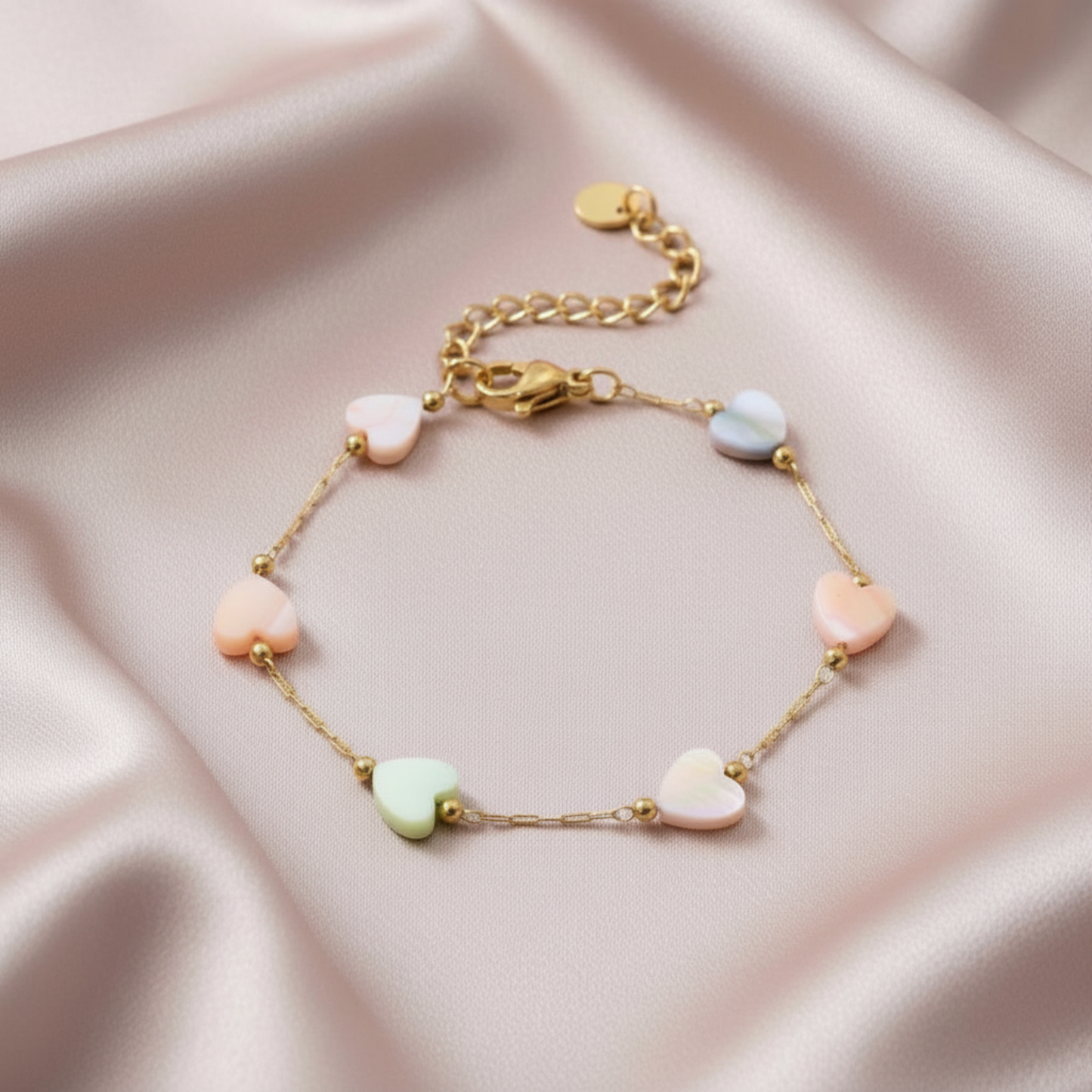 Gold bracelet with heart-shaped beads on a pink satin background