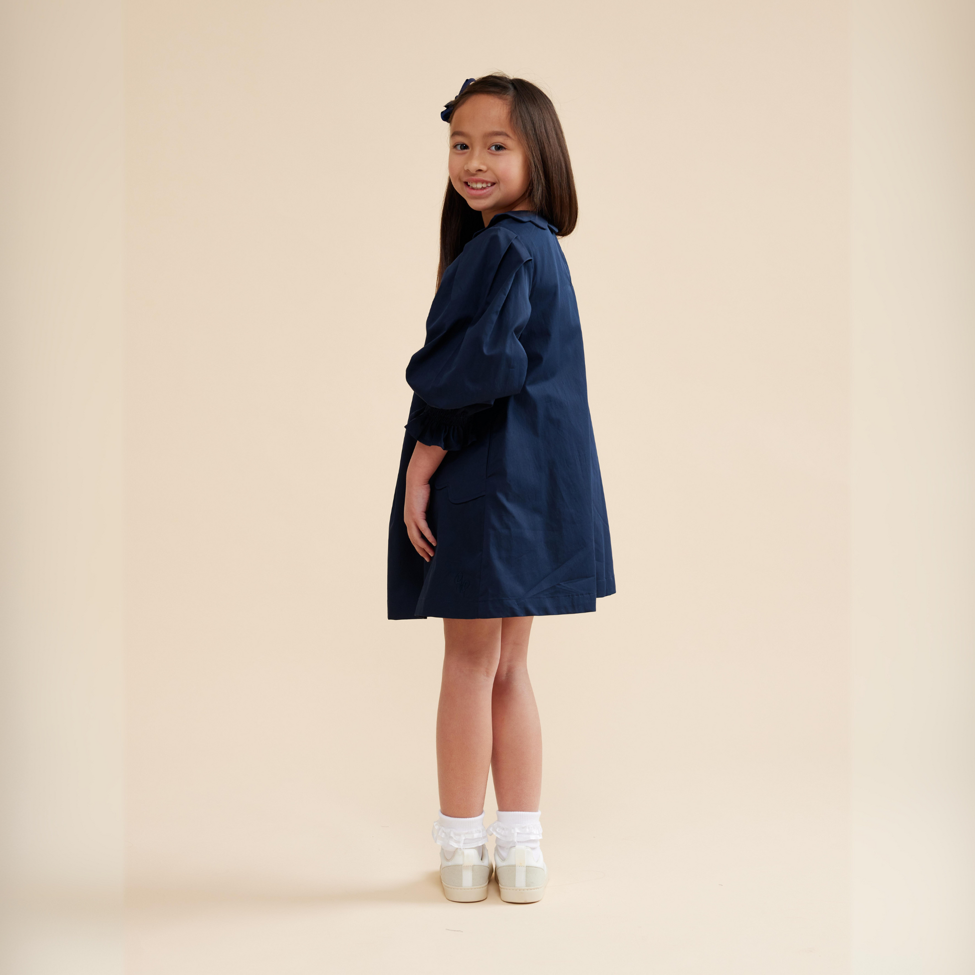 Girl wearing navy scallop detail smock dress styled with sneakers