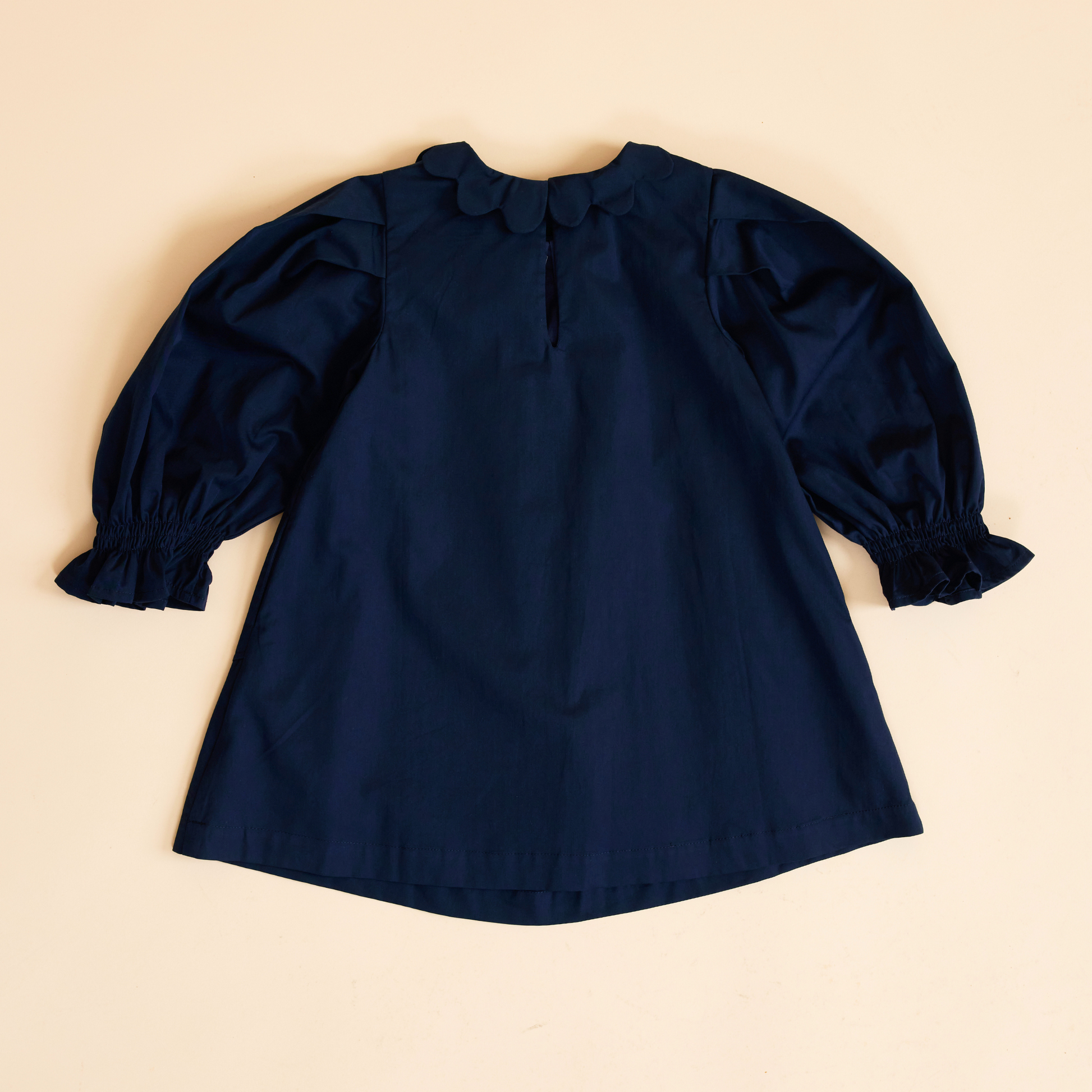 Back view of navy scallop detail smock dress with long sleeve and shirred gathered cuffs, scallop collar and pocket details, A-line shape and soft cotton fabric