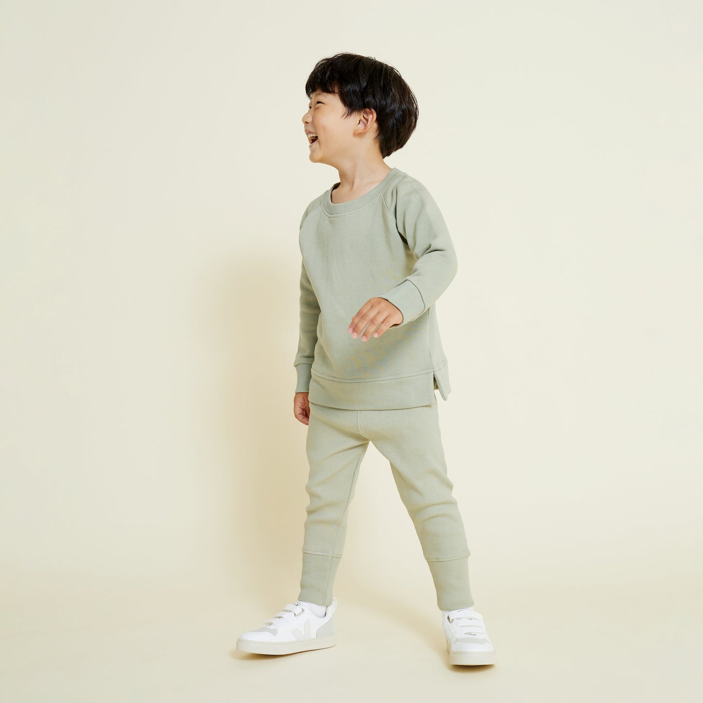 A child wearing a sage green sweatshirt and matching leggingspaired with white Veja sneakers