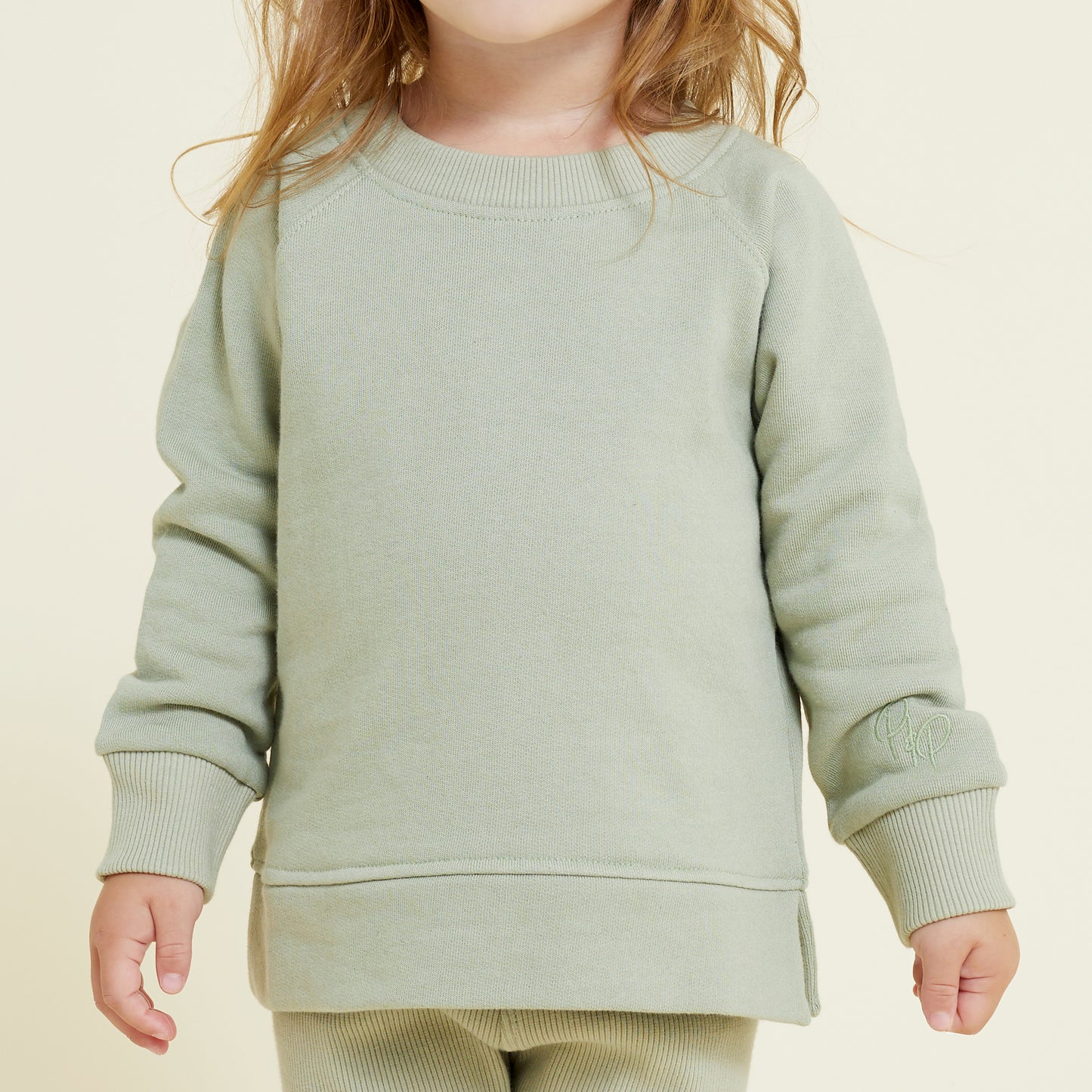 Front detail image of sage green sweatshirt, showing ribbed collar and cuffs and embroidery detail. Worn by a little girl.