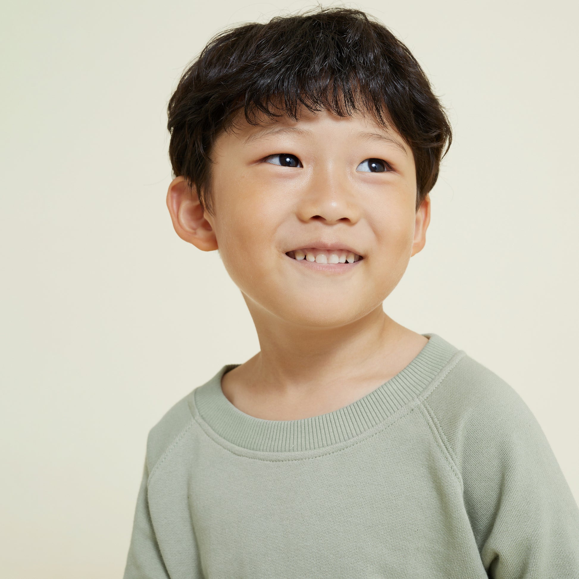 Close up image of 5 year old boy wearing sage green sweatshirt smiling for the camera