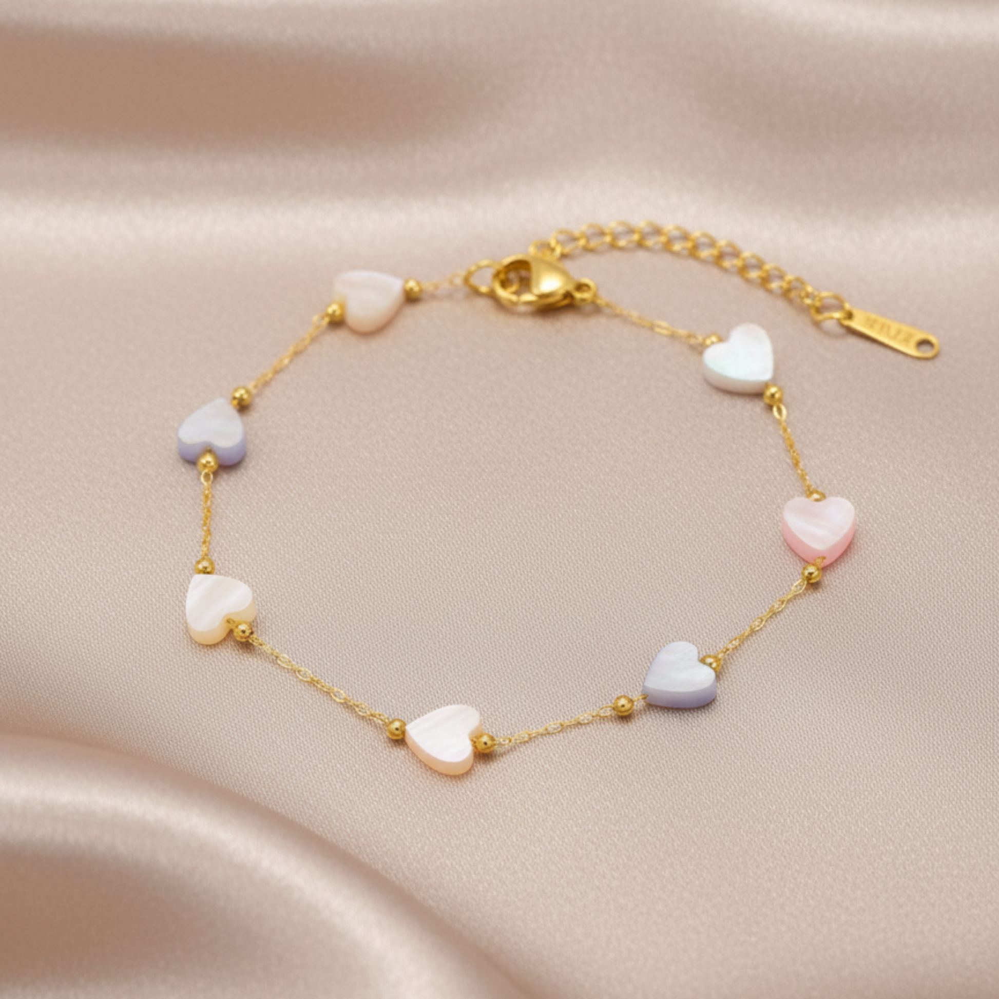 Gold bracelet with heart-shaped beads on a beige fabric background