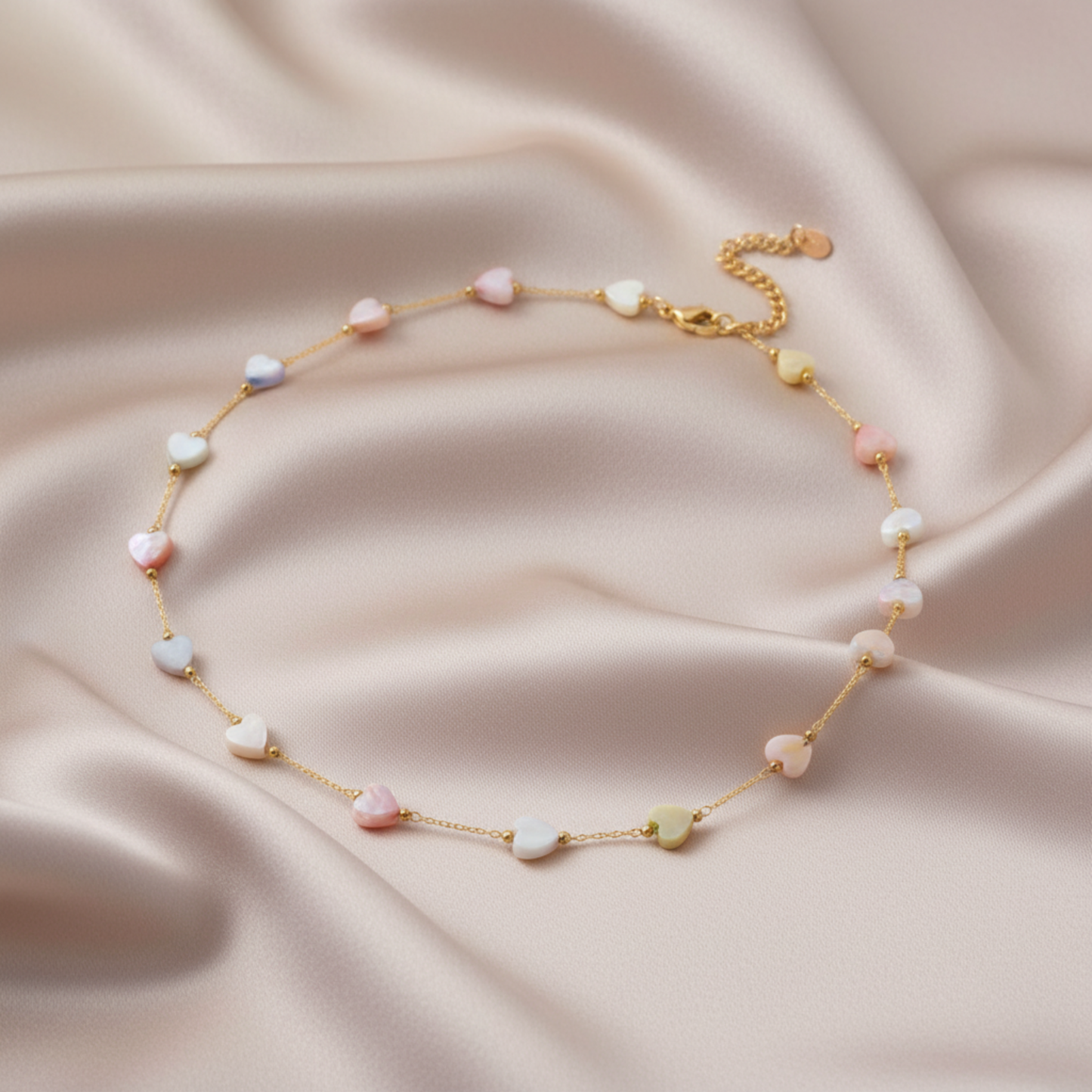 Delicate gold bracelet with colorful beads on a soft pink fabric background