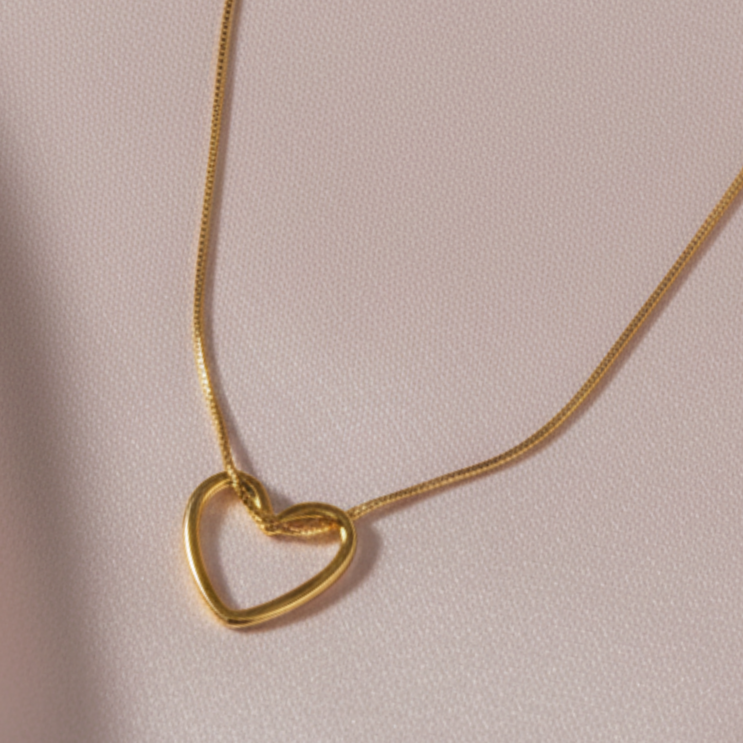 A close up image of fine gold love heart hangs from a delicate gold chain