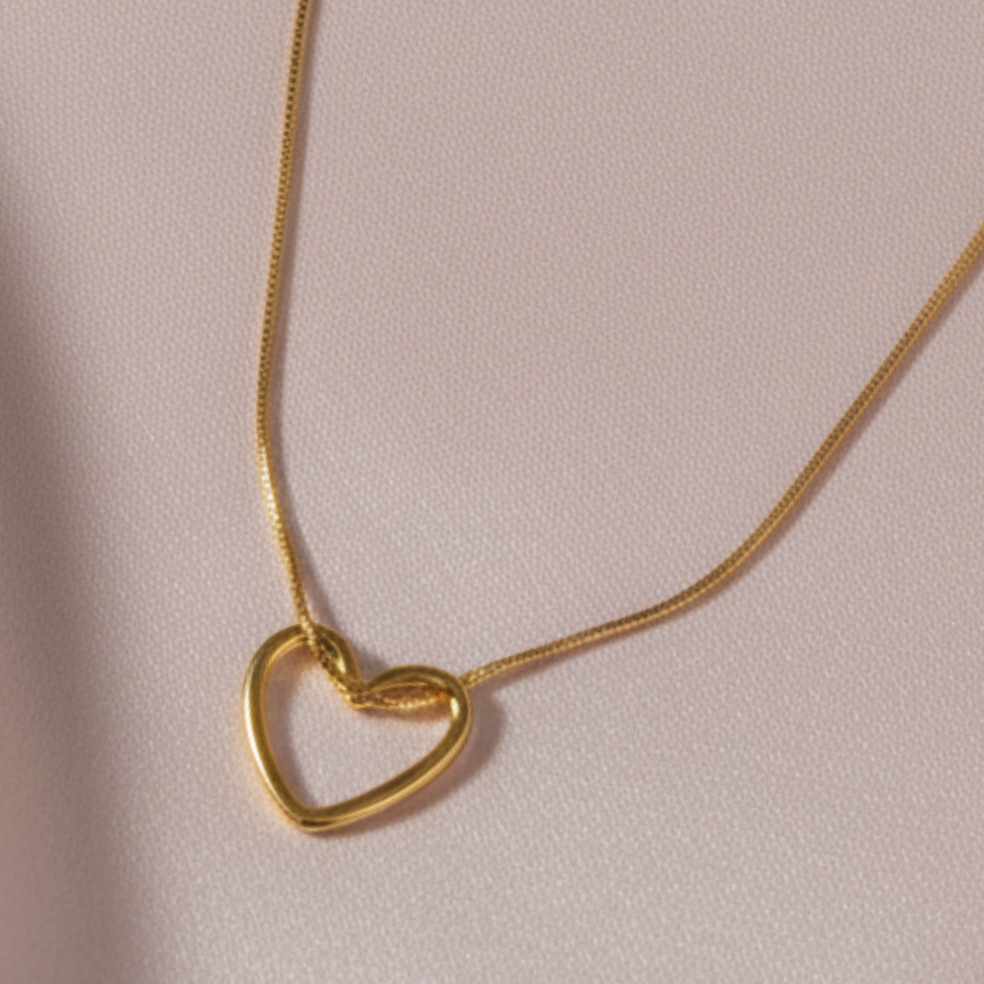 A close up image of fine gold love heart hangs from a delicate gold chain
